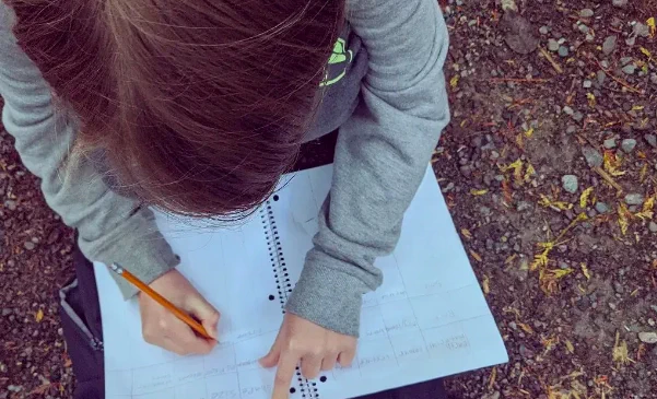 A child sitting down outside writing in their notebook