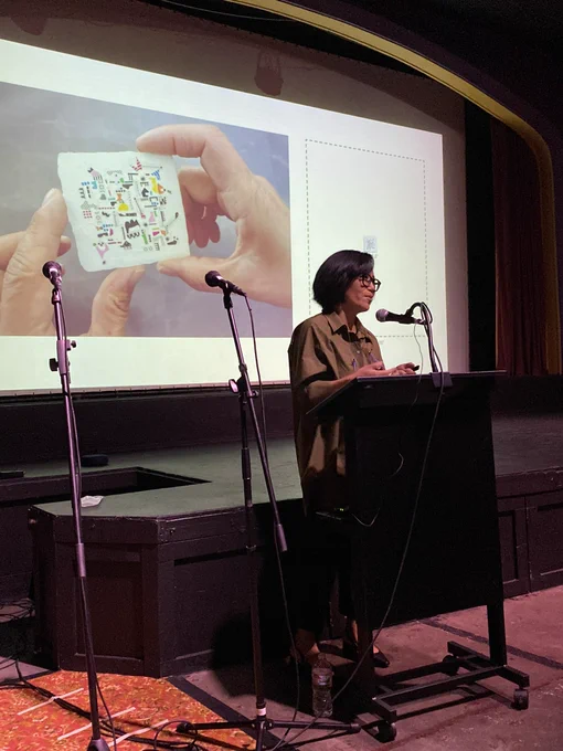 Visual artist Yoonhee Choi speaking in front of a projected image of one of her pieces.