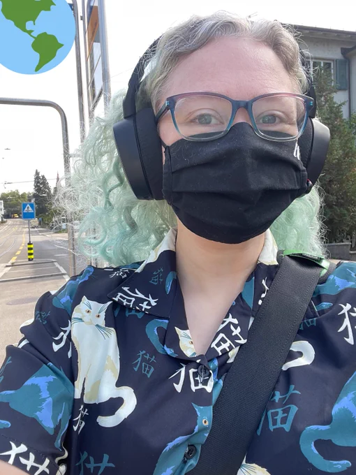 Selfie of a person with seafoam-coloured hair, wearing a face mask and a shirt with cats on it.