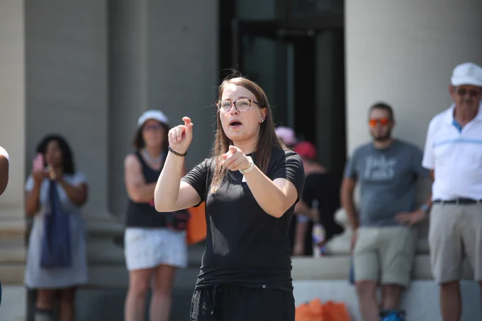 Sign language interpreter signing on stage with a crowd behind her at the Missouri History Museum