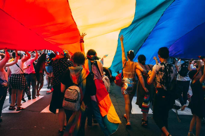Menschen laufen unter einer großen Regenbogenflagge. 