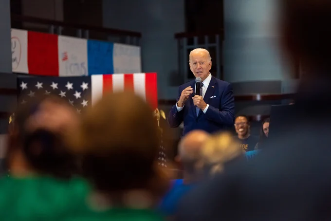 President Biden holding a microphone and speaking to a crowd at the National Education Association headquarters