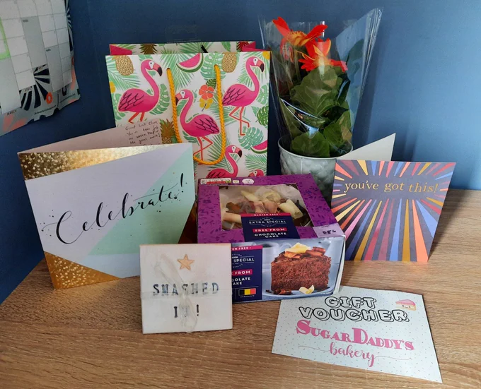Cards and gifts I got from my educator and the team including a chocolate cake, a gift voucher for Sugar Daddies bakery, a coaster that says "smashed it" on it and a gerbera plant in a pot