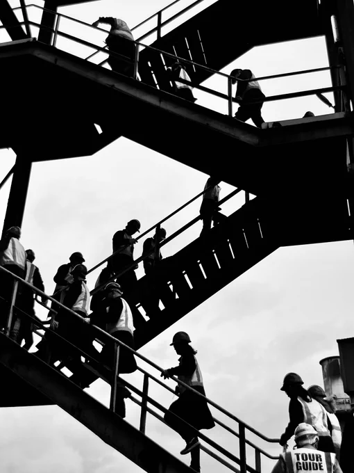 A black-and-white photo of a tour group ascending a set of industrial stairs