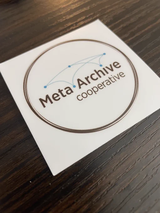 Close up of MetaArchive sticker, MetaArchive logo in concentric brown circles on white background.