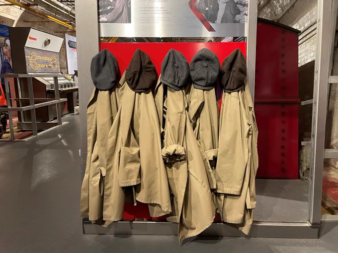 Image shows the old postal workers' brown jackets and caps hanging up in a row on pegs.