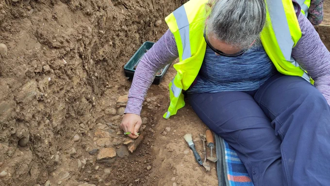 Volunteer carefully excavating a mass of pot fragments from the stoney ground.