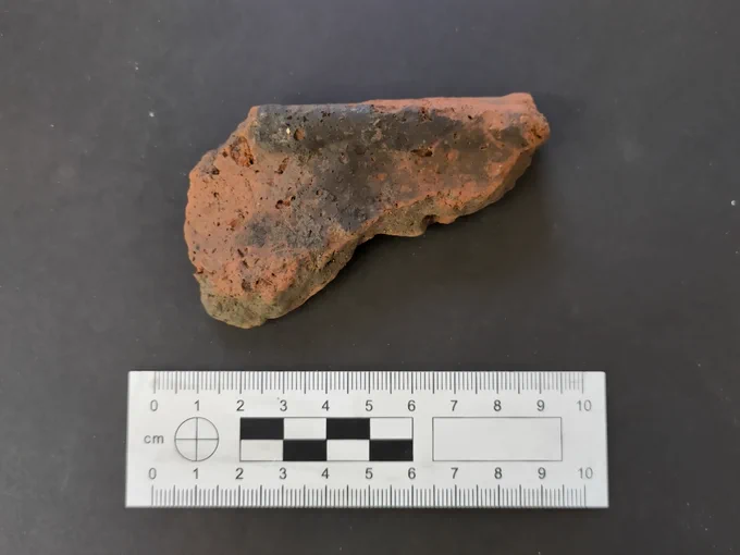 Early Iron Age pot rim with scale, showing that fragment is about 9cm long. Pot had an uneven red surface with a burnt black patch.