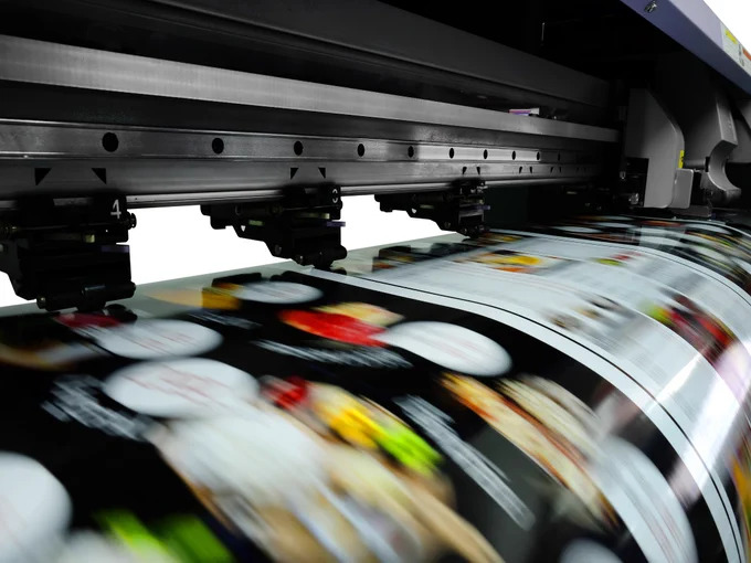 A close-up of the creation of a print in an industrial inkjet. The print is motion blurred and its design is unclear. However, the machinery is visible.