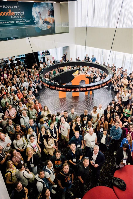 A big room full of MoodleMoot Global attendees, in a shot taken from above. Everyone is looking at the camera and smiling