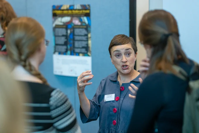 student standing next to their poster and talking to another student