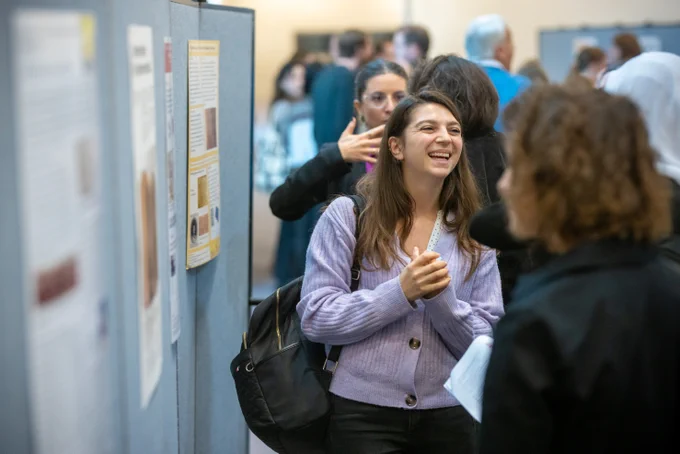 smiling student standing next to their poster and talking to other people 