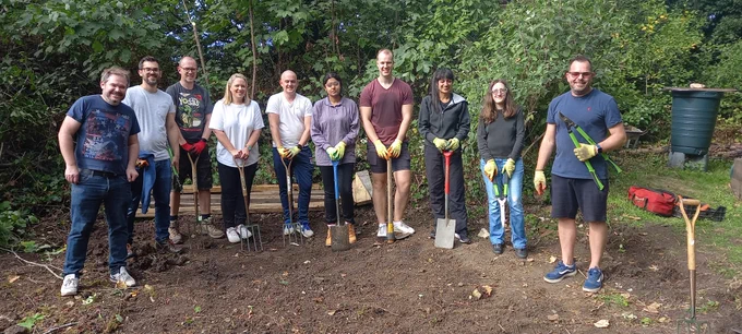 Group photo of corporate volunteers from TMHCC with spades in their hands in a park.