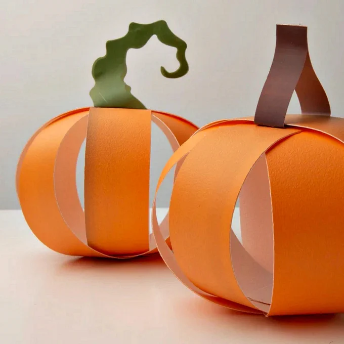 two craft pumpkins made of paper strips, one with green stem and one with brown stem