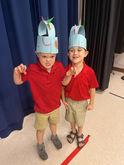 Image of 2 boys wearing dinosaur crafts on their heads and posing like dinosuars 