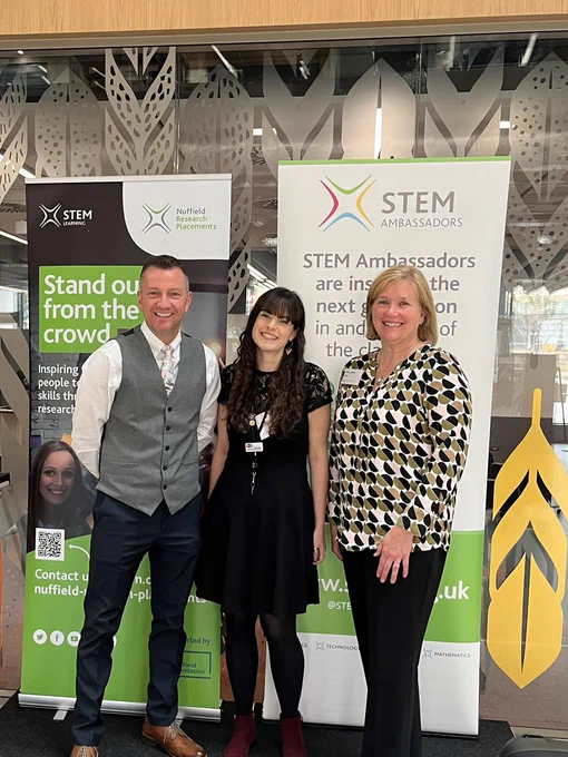 Three SSERC staff posing on stage with the Nuffield Research Placements banner