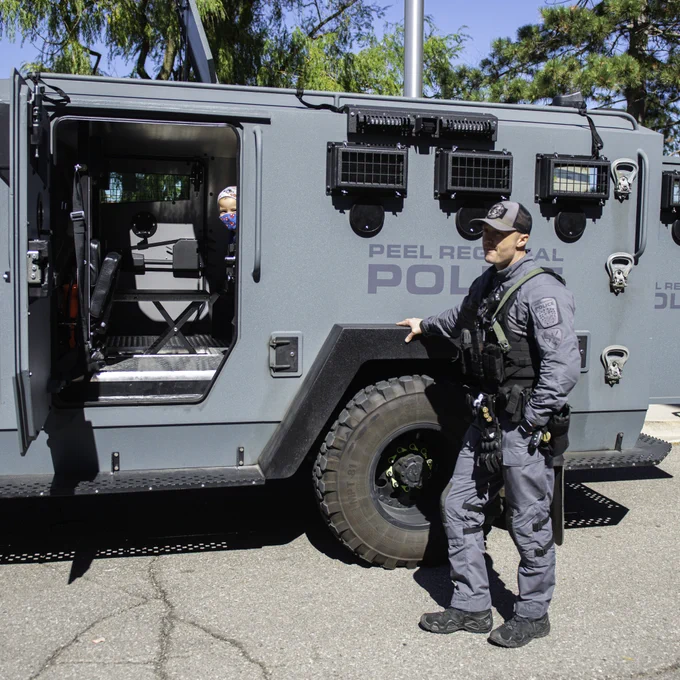 Photo of a small boy inside of a Peel Regional Police swat cruiser with police man standing outside.