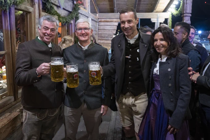 Tim holds a beer and smiles for a group photo in Munich at Wiesn, also known as Oktoberfest. People are dressed in traditional garb and hold full beer steins.