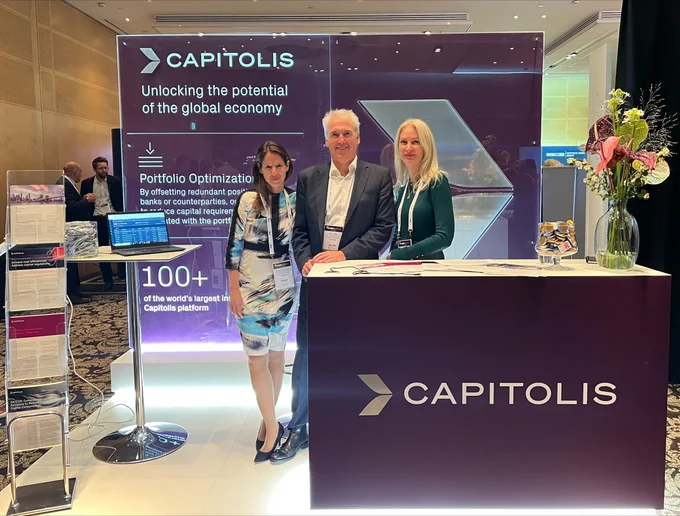 A woman, man, and woman standing up side-by-side in front of a booth that reads "Capitolis". 