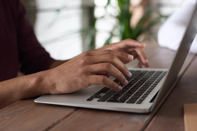 Hands typing on a laptop that is sitting on a wood table.