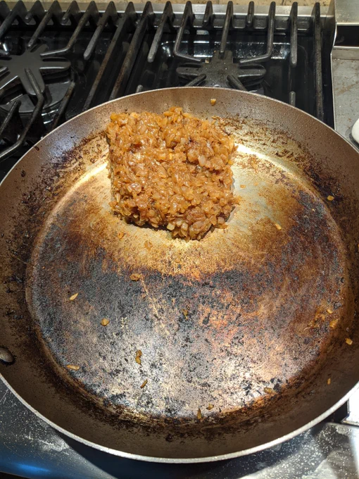 3 caramelized onions in a stainless steel skillet that has considerable discoloration from cooking the onions down.