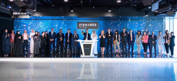 21Shares CEO and team complete the bell-ringing ceremony as Nasdaq Dubai, celebrating the launch of the regions first ever BTC backed ETP. There are many people lined across the stage clapping, cheering, and celebrating this historic moment while confetti rains down.