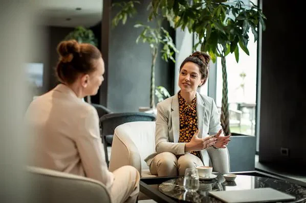 Two professionals wearing a pant suit sitting and chatting