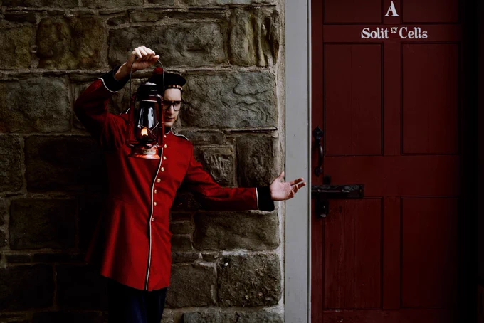 A 19th century British soldier stands in front of the solitary cell room door of the guard house in downtown Fredericton, with a lantern raised high.