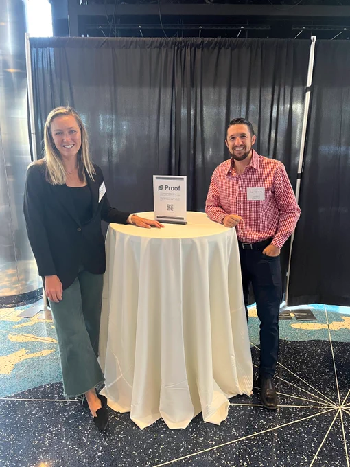 Photo of Proof team members next to Proof table sign