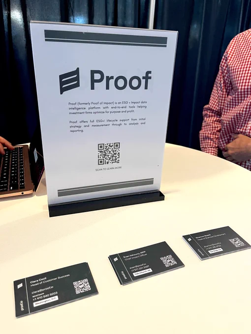 Photo of table sign displaying Proof logo and QR code with business cards of team members set in front