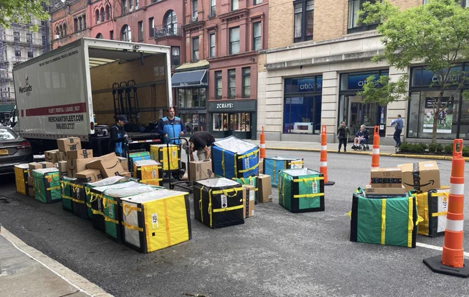 A delivery truck double parked with large area on the street taken up by delivery packages.
