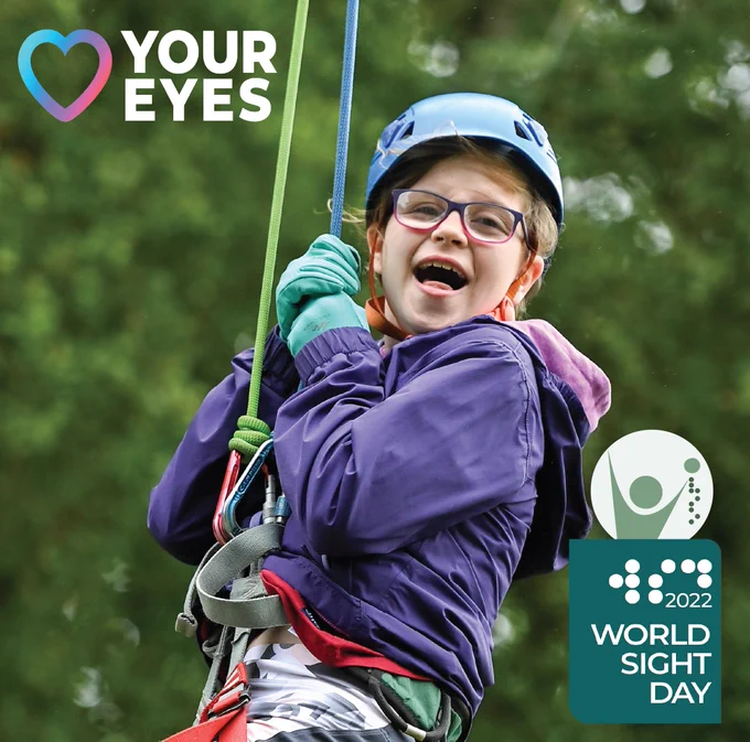 Photo of girl zip lining smiling wearing a purple coat and blue helmet. Photo includes Love Your Eyes branding and World Sight Day logo.