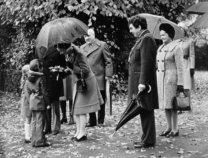 Black and white photograph of Queen Elizabeth II accepting flowers from a child while holding an umbrella.