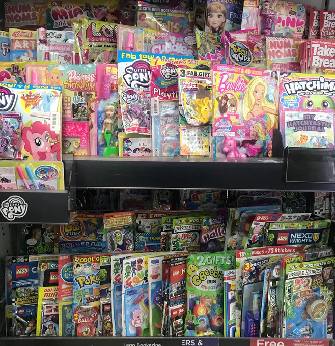 two rows of magazines on supermarket shelves. The majority of them have plastic tat (toys, games etc) on the front. And most are also wrapped in plastic.