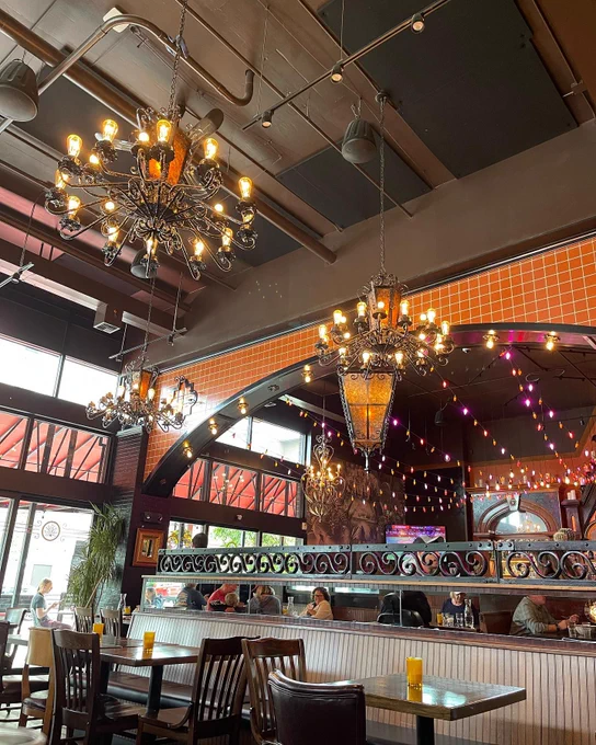 The interior of Poquitos Bothell, with two tables in the foreground and faux candle chandeliers hanging from the ceiling. An orange arch is in the background.
