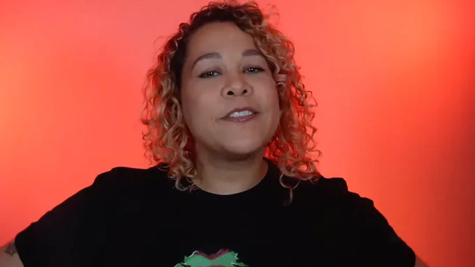 An image of creator Cris Alex in front of a red background, smiling, wearing a black t-shirt.