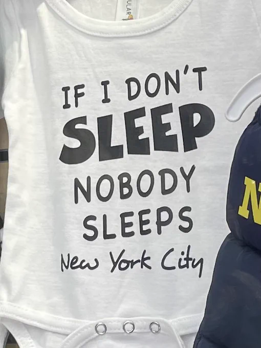 A toddler’s onesie outfit, it has text that reads “IF I DON’T SLEEP / NOBODY SLEEPS / New York City
