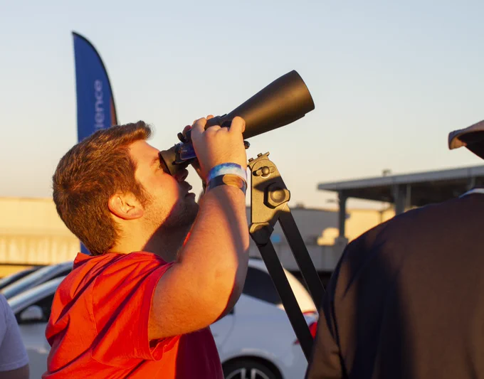 A male student looks through a set of high powered binoculars at the moon.