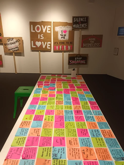 a table if bright post it note messages with protest placards in background 