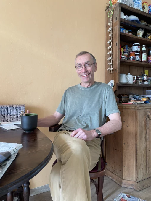 2022 medicine laureate Svante Pääbo sitting at a table drinking a cup of coffee. He is smiling.
