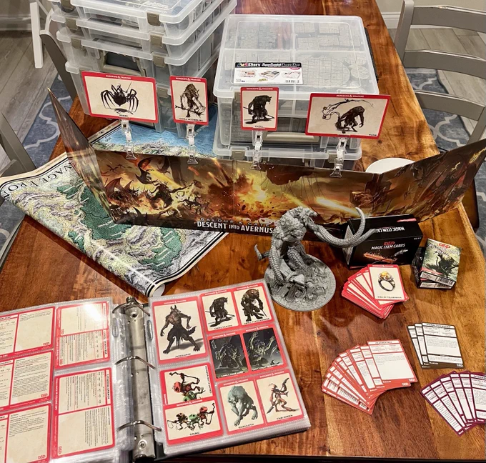 Big pile of D&D products on a table: a binder of monster cards, stacks of reference cards, poster maps, a Descent into Avernus DM screen, craft dividers full of miniatures and dungeon tiles, and an 8-inch model of Demogorgon, Prince of Demons.