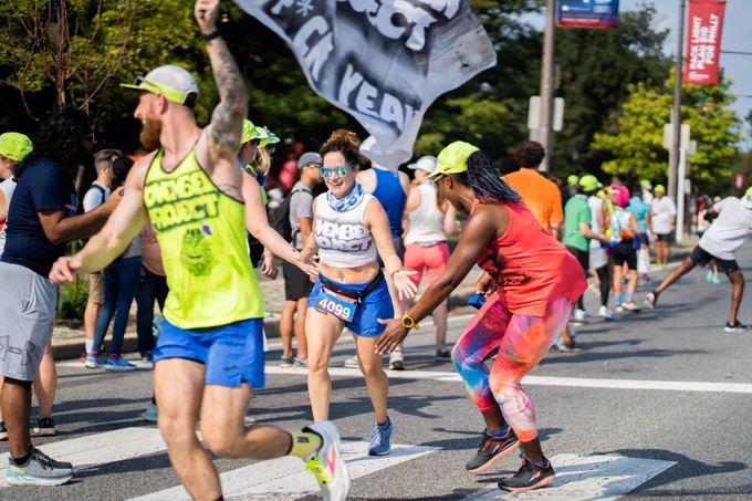 November Project member running through a cheer station with one supporter leading them by waiving November Project flag and the other one high-fiving them off to the side. 