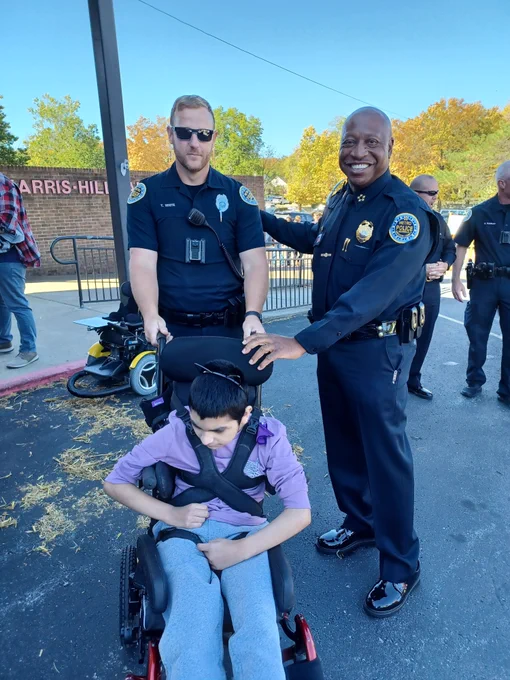 Police officer and Chief Drake pose for photo with a student using a wheelchair.