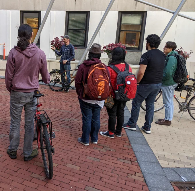 people with backpacks looking at person with bike