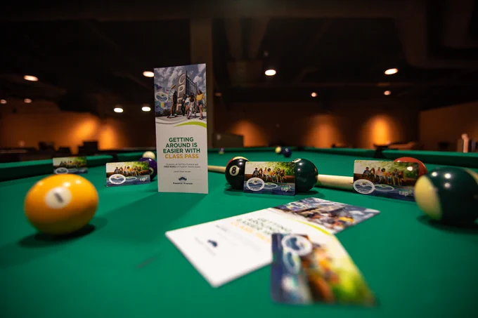 A Class Pass Brochure and Class Pass TAP Card displayed on a pool table surrounded by pool equipment in the Games Room Etc. 