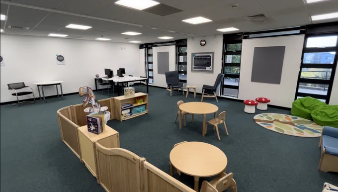 Ground floor room with low tables and chairs, a rug, bean bags, a paper dinosaur and other things for kids