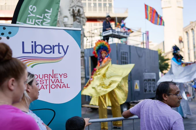 An image of performers on an outdoor square with the Liberty EU and Journeys Festival International banners on the left side. Image by Pete Martin Photography.