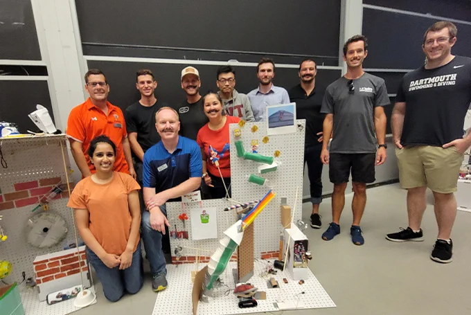 A group of students standing around a complicated "Rube Goldberg" device.