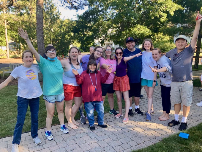 Group of adults grouped together outside with smiles and some waving.
