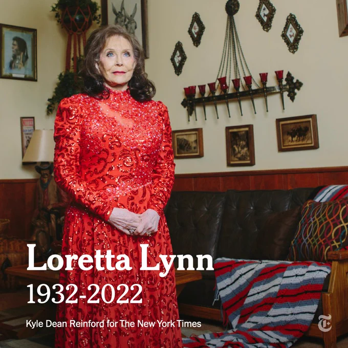 Loretta Lynn: 1932-2022. She wears a sparkling red gown and stands with her hands clasped, looking out in the distance, inside her Tennessee ranch home. Photo by Kyle Dean Reinford for The New York Times.